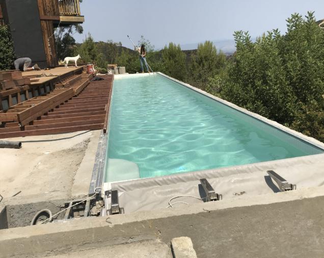 A sleek, long lap pool under construction on a hillside property, surrounded by greenery.
