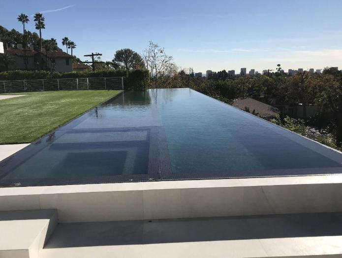 An infinity pool overlooking the city skyline with a lush green lawn beside it.