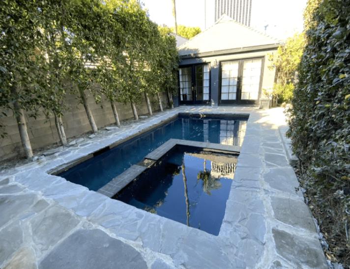 A private rectangular pool with a built-in spa, surrounded by lush greenery and stone flooring in Pasadena.