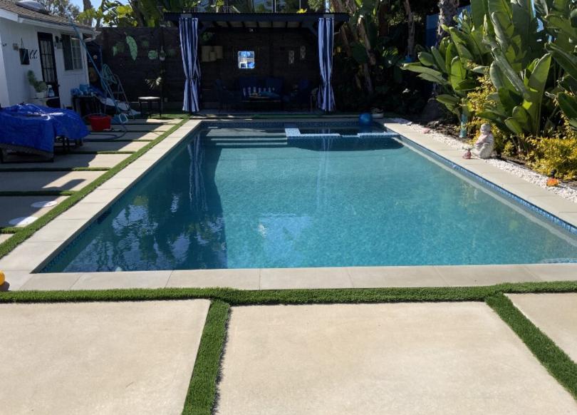 A backyard pool with a natural stone spa, surrounded by landscaping and a cozy patio area.