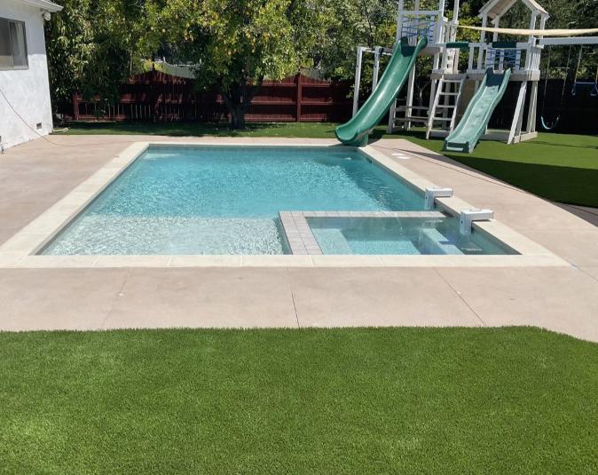 A backyard swimming pool with a built-in shallow section, slides, and a play area.