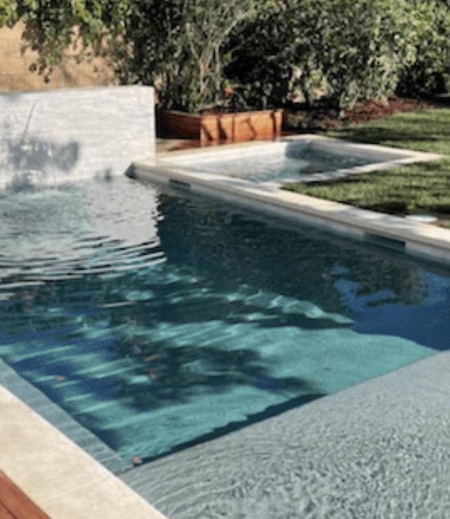 A modern swimming pool with a shallow lounge area, spa, and a cascading water feature in Pasadena.